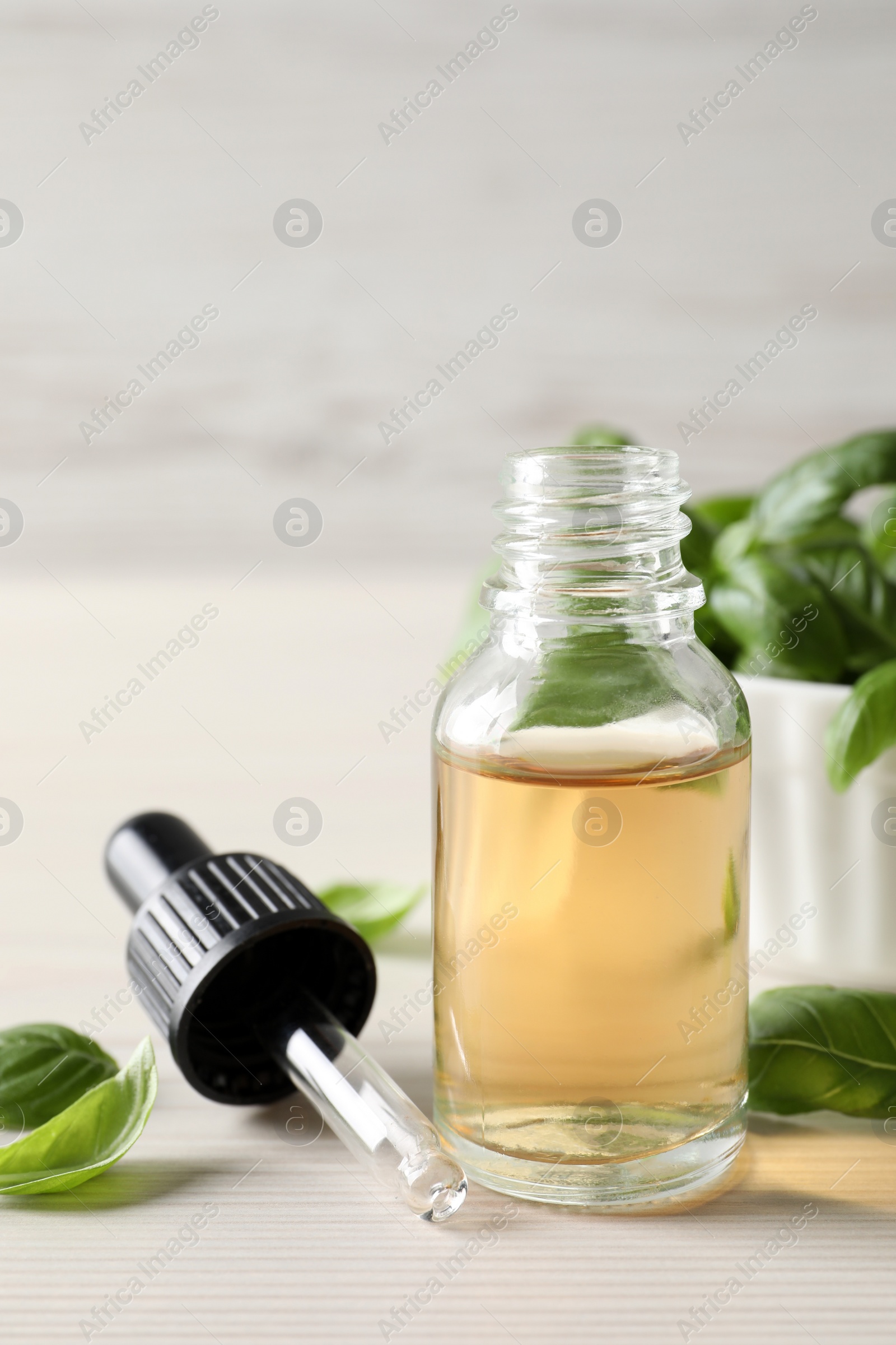 Photo of Glass bottle of basil essential oil and leaves on white table