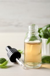 Photo of Glass bottle of basil essential oil and leaves on white table