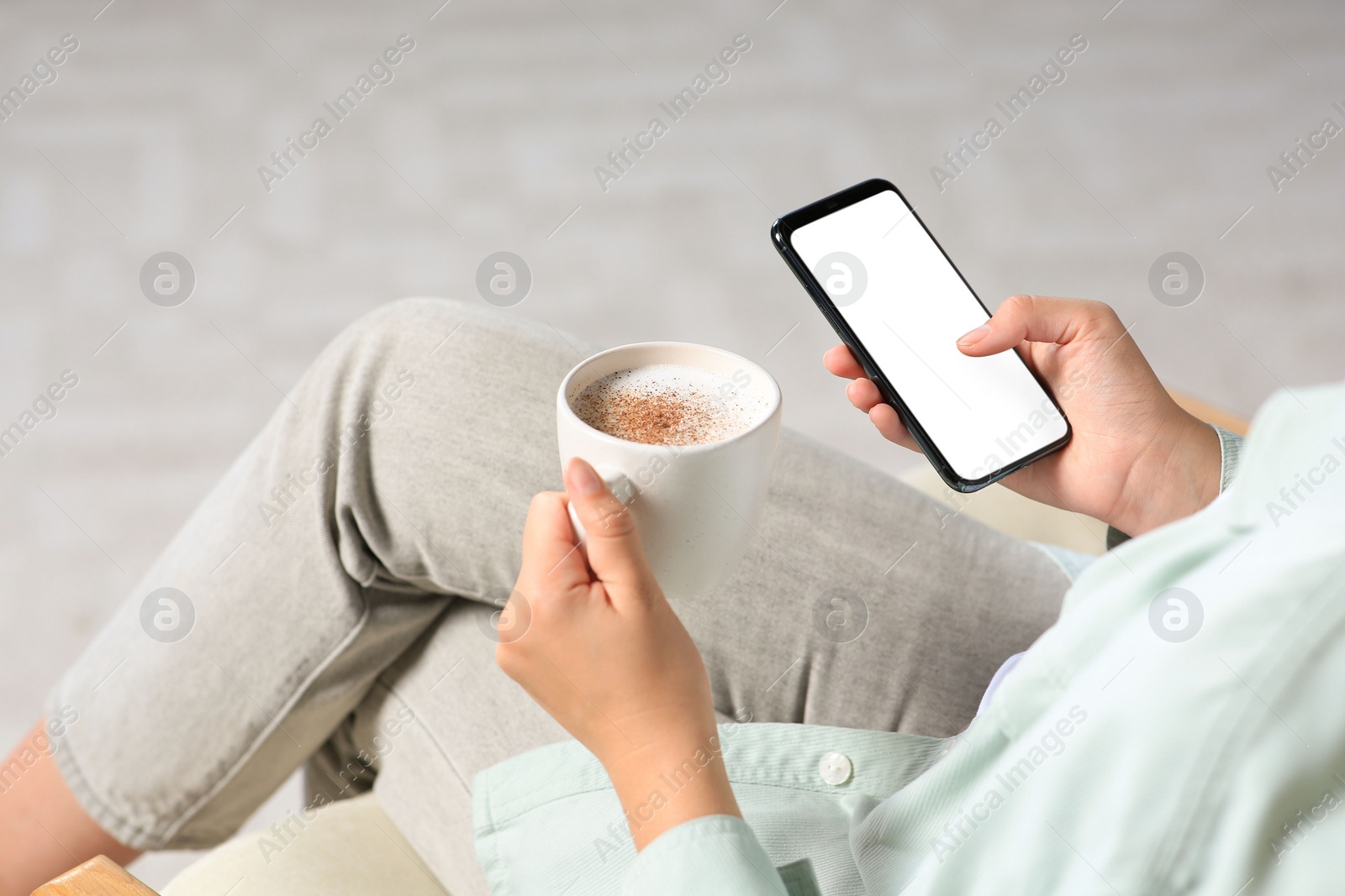 Photo of Woman with smartphone and cup of coffee indoors, closeup