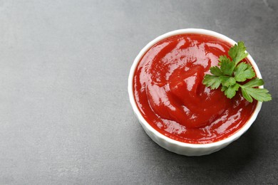 Photo of Delicious tomato ketchup and parsley in bowl on grey textured table, closeup. Space for text