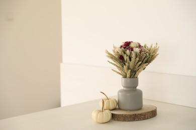 Photo of Beautiful bouquet of dry flowers in vase and small pumpkins on white table indoors, space for text