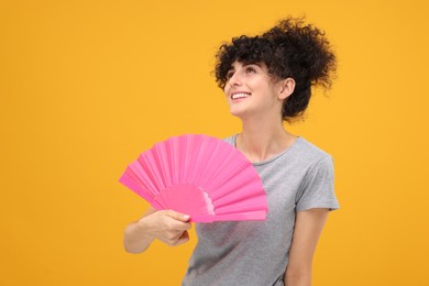 Photo of Happy woman holding hand fan on orange background. Space for text