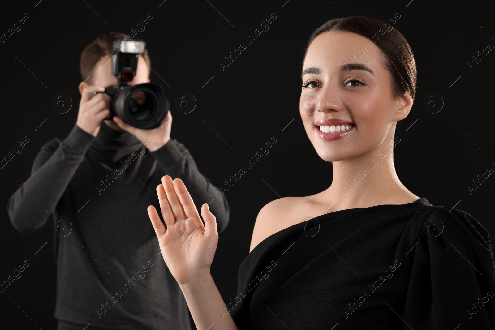 Photo of Photographer taking picture of beautiful woman on black background, selective focus