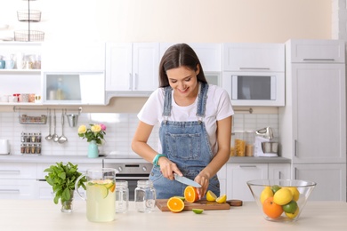 Young woman preparing lemonade on table in kitchen. Natural detox drink