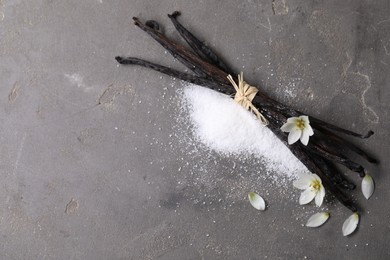 Vanilla pods, sugar, flowers and petals on gray textured table, flat lay. Space for text