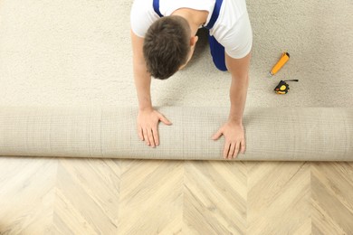 Photo of Worker rolling out new carpet flooring indoors, top view