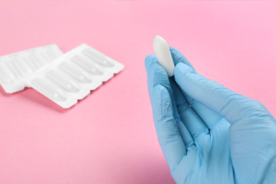 Photo of Woman holding suppository on pink background, closeup. Hemorrhoid treatment