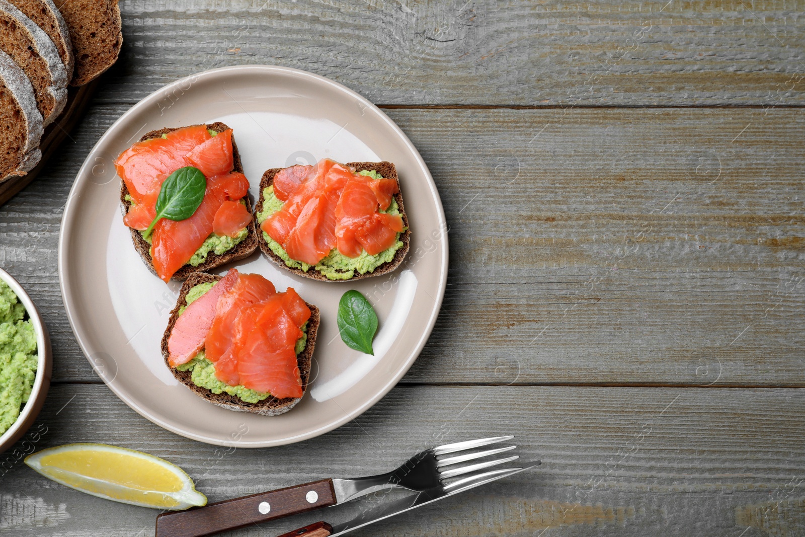 Photo of Delicious sandwiches with salmon and avocado served on grey wooden table, flat lay. Space for text