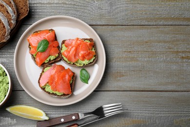 Photo of Delicious sandwiches with salmon and avocado served on grey wooden table, flat lay. Space for text