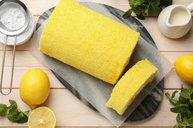 Delicious cake roll, lemons, mint and powdered sugar on light wooden table, flat lay