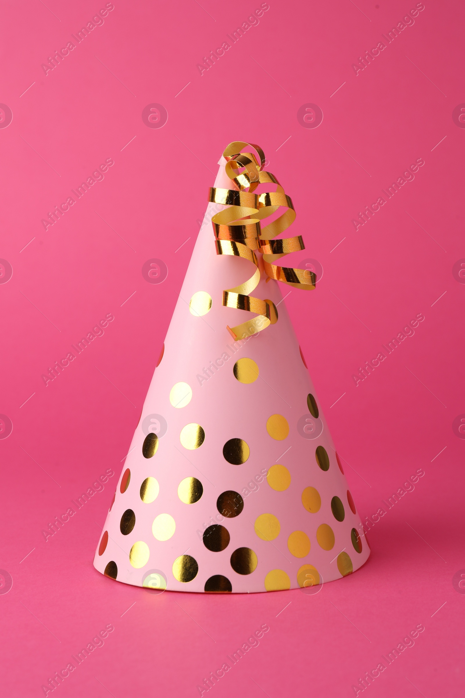 Photo of One beautiful party hat with serpentine streamers on pink background