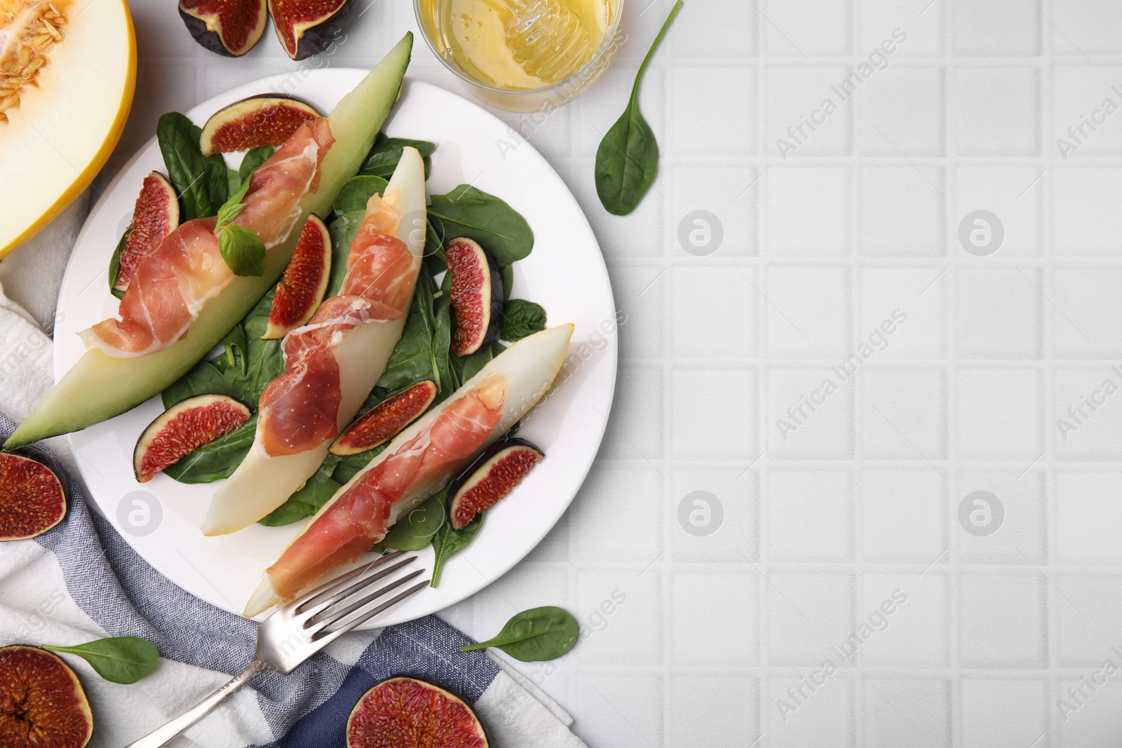 Photo of Tasty melon, jamon and figs served on white tiled table, flat lay. Space for text