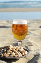 Photo of Glass of cold beer and pistachios on sandy beach near sea
