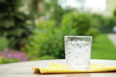 Photo of Glass of fresh water on wooden table outdoors, space for text
