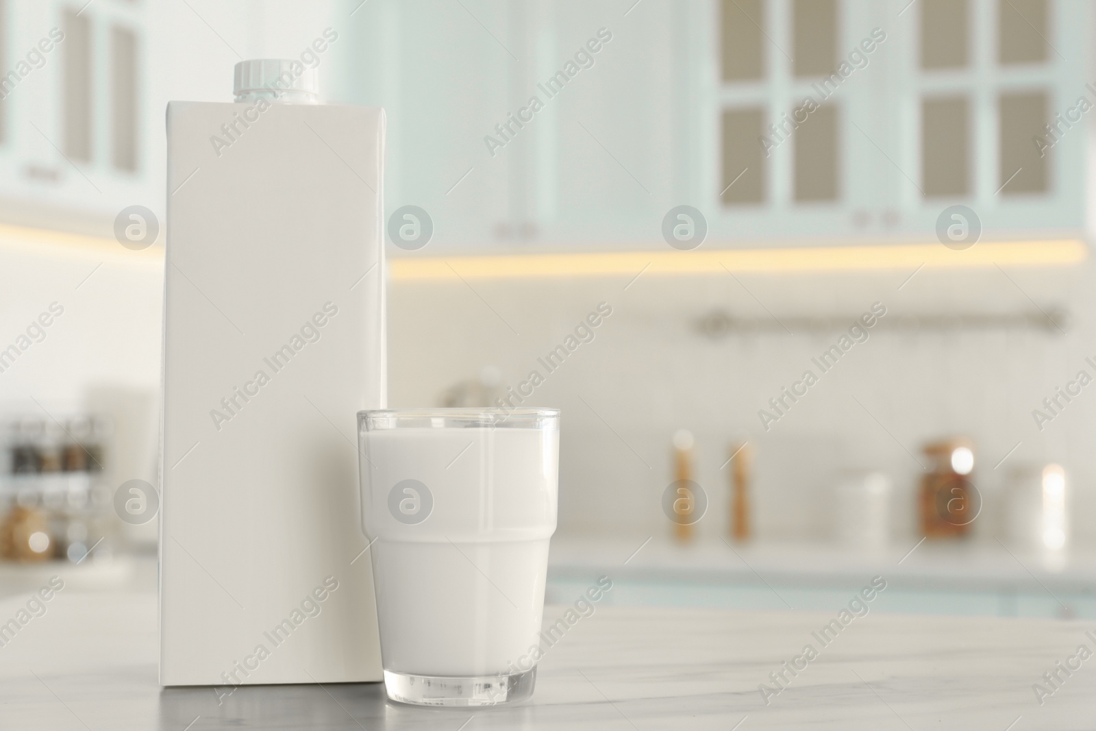 Photo of Carton box and glass of milk on table in kitchen, space for text