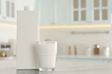 Photo of Carton box and glass of milk on table in kitchen, space for text