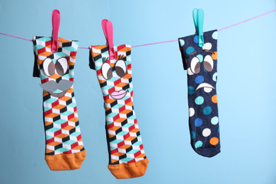 Photo of Socks with faces hanging on rope against light blue background. Concept of jealousy