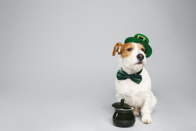 Photo of Jack Russell terrier with leprechaun hat, bow tie and pot on light grey background, space for text. St. Patrick's Day