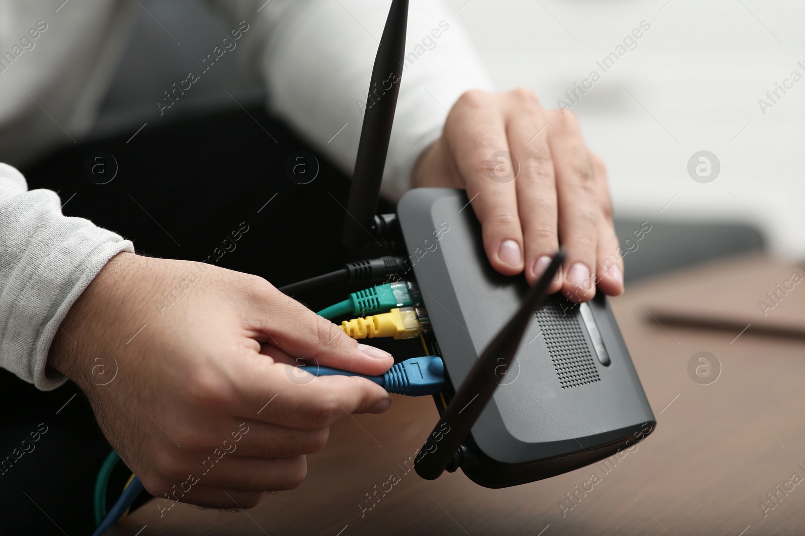 Photo of Man inserting cable into Wi-Fi router at wooden table indoors, closeup