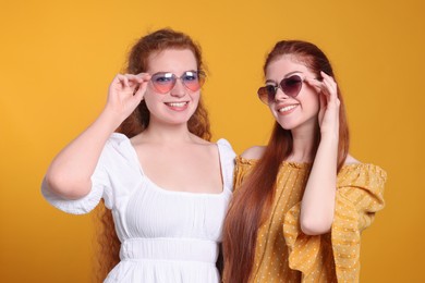 Photo of Portrait of beautiful young redhead sisters with sunglasses on orange background