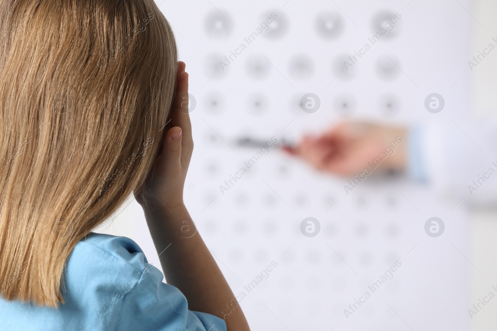 Photo of Ophthalmologist testing little girl's vision in clinic, back view