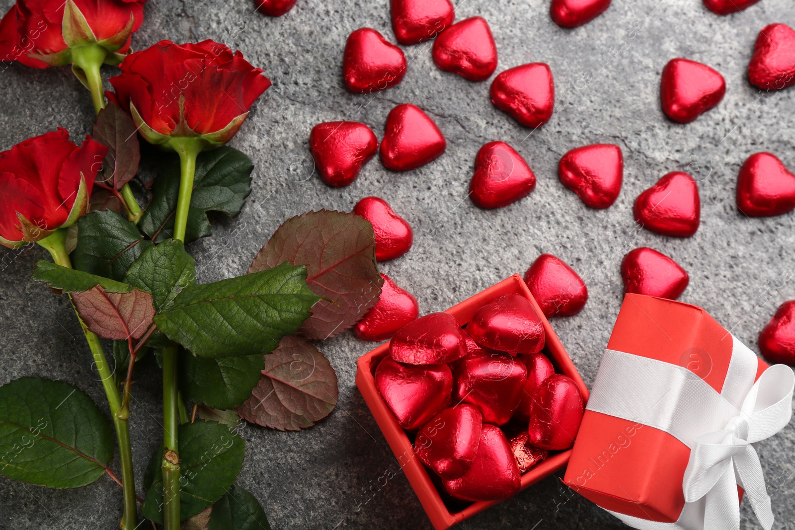 Photo of Heart shaped chocolate candies, gift box and bouquet on grey table, flat lay