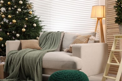 Photo of Sofa near Christmas tree in room. Festive interior design
