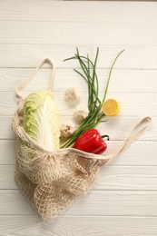 Photo of Fresh ripe Chinese cabbage and other vegetables in net bag on white wooden table, top view