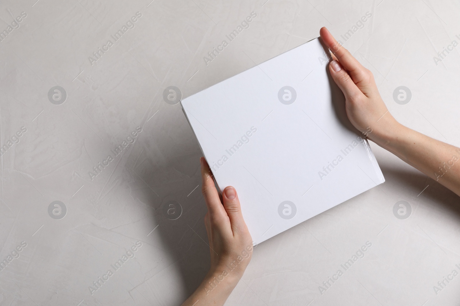 Photo of Woman holding book with blank cover at white table, top view. Mockup for design