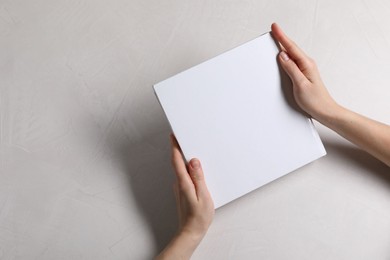 Photo of Woman holding book with blank cover at white table, top view. Mockup for design