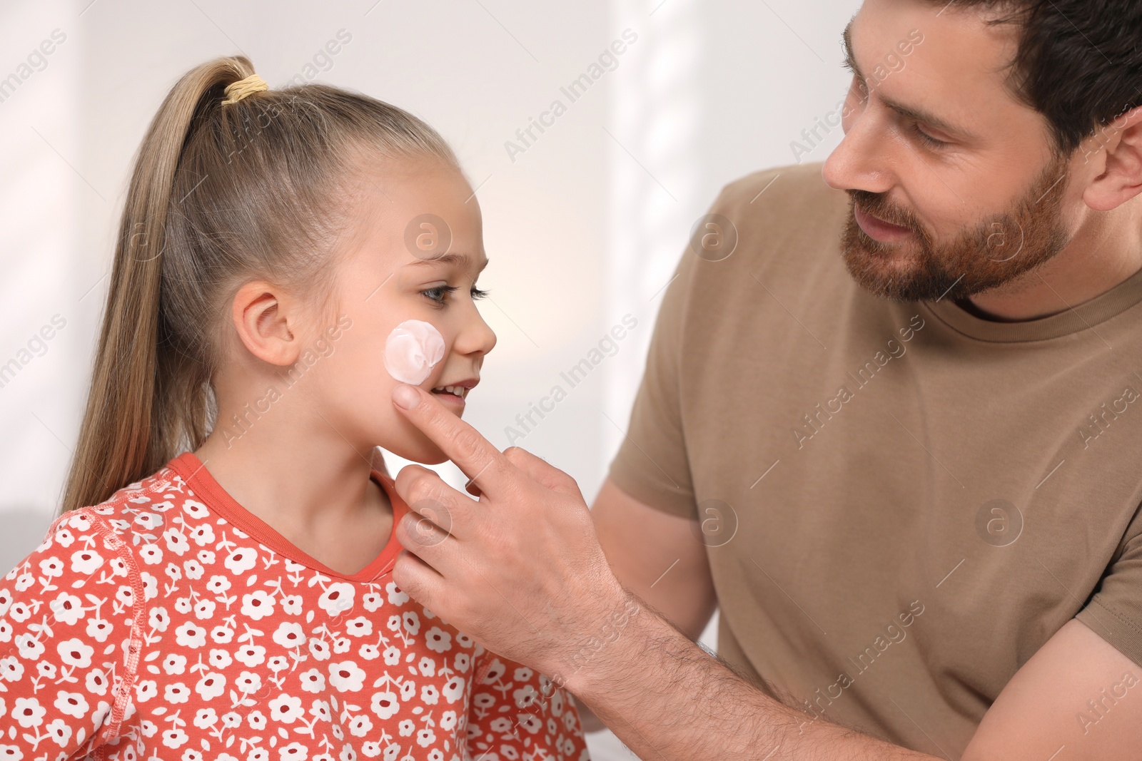 Photo of Father applying ointment onto his daughter's cheek on white background