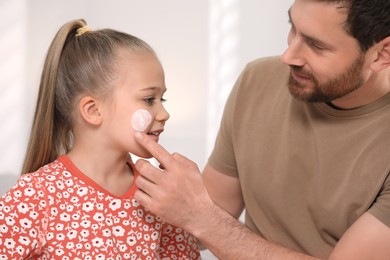 Father applying ointment onto his daughter's cheek on white background