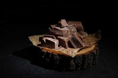 Photo of Pieces of tasty milk chocolate on wooden board, closeup