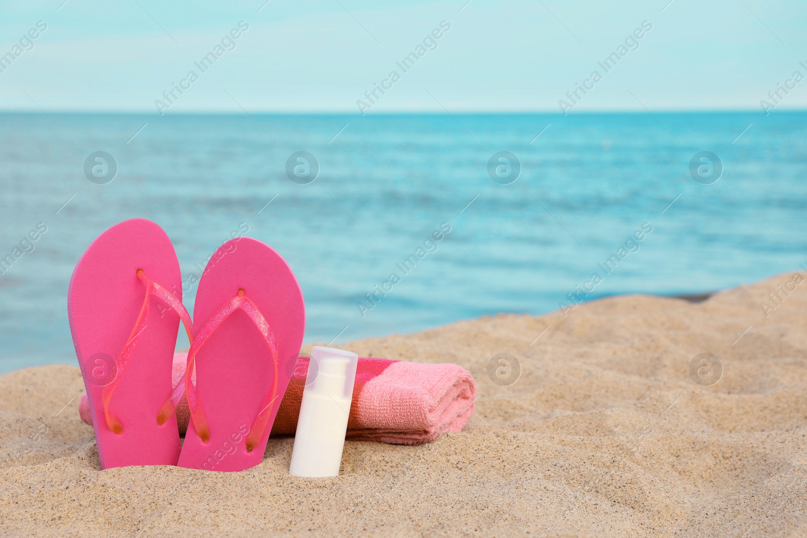 Photo of Beach towel, slippers and sunscreen on sand near sea, space for text