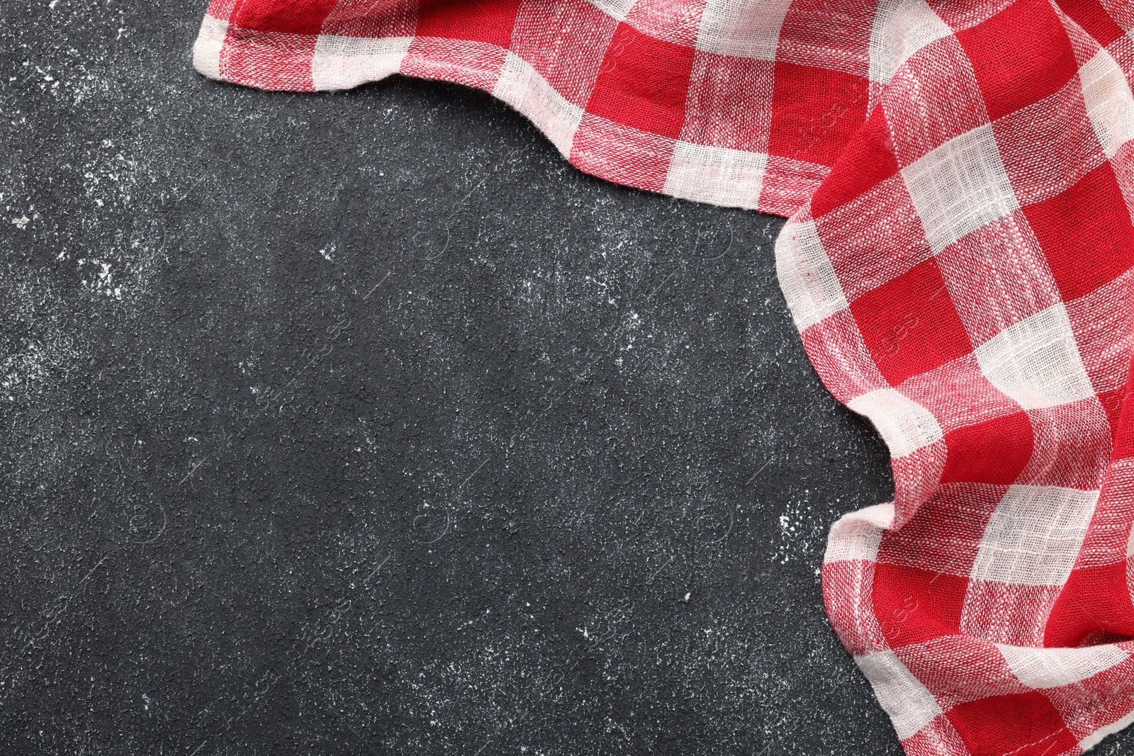 Photo of Red checkered tablecloth on black textured table, top view. Space for text