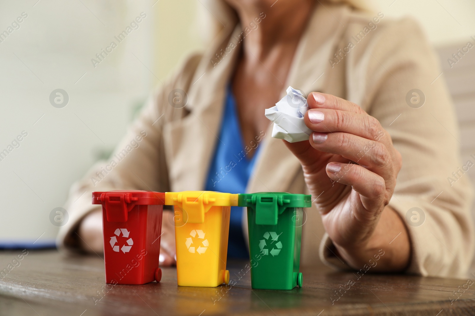 Photo of Woman throwing paper into mini recycling bin at office, closeup