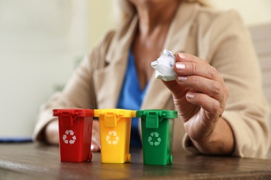 Woman throwing paper into mini recycling bin at office, closeup