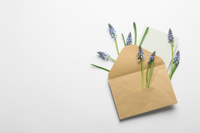 Envelope with beautiful spring muscari flowers and card on light background, flat lay. Space for text