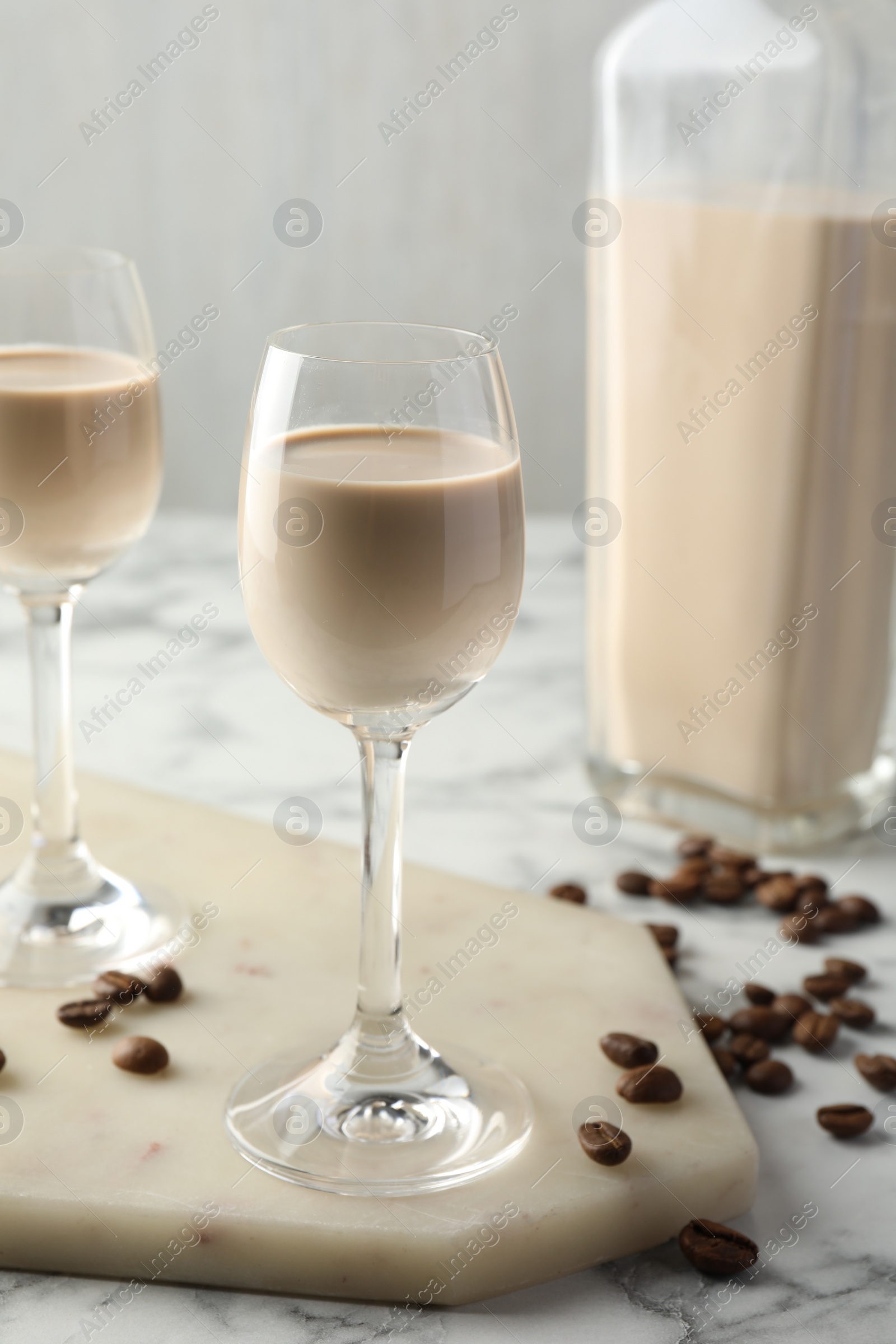 Photo of Coffee cream liqueur in glasses, beans and bottle on white marble table