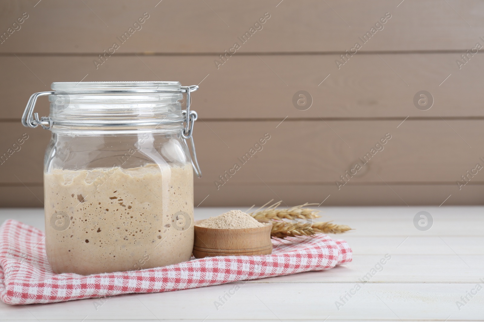 Photo of Leaven and ears of wheat on white wooden table, space for text