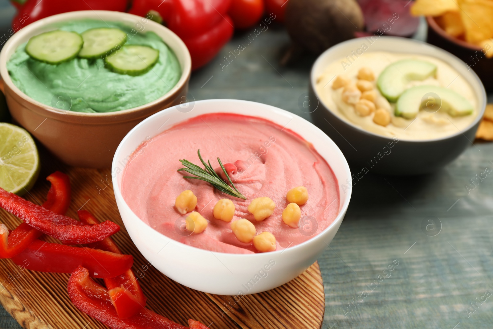 Photo of Different kinds of tasty hummus with ingredients on light blue wooden table