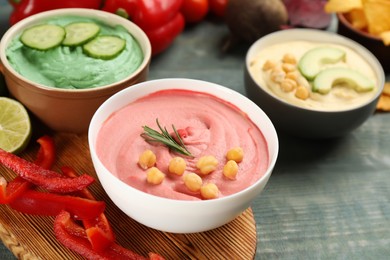 Photo of Different kinds of tasty hummus with ingredients on light blue wooden table