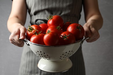 Woman with colander of ripe tomatoes on grey background, closeup