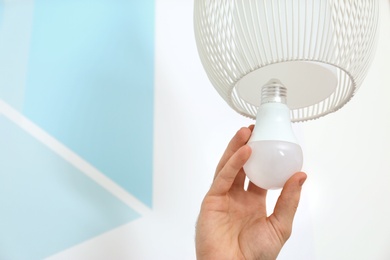 Photo of Man changing light bulb in lamp against color wall, closeup. Space for text