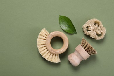 Photo of Cleaning brushes, loofah and leaf on green background, flat lay. Space for text