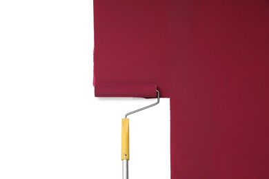 Applying burgundy paint with roller brush on white wall