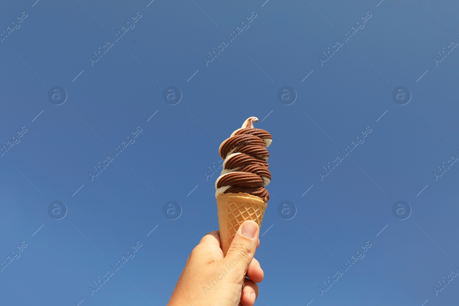 Photo of Woman holding delicious ice cream in wafer cone against blue sky, closeup