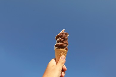 Woman holding delicious ice cream in wafer cone against blue sky, closeup