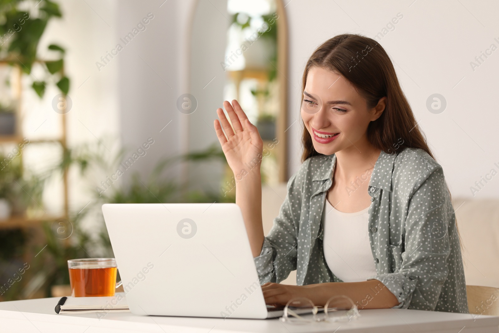 Photo of Happy young woman having video chat on laptop at table indoors