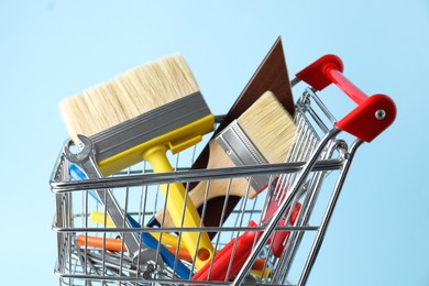 Photo of Different construction tools in shopping cart on light blue background, closeup